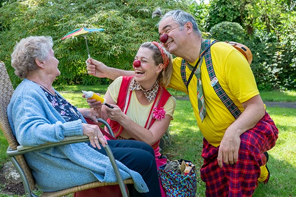 Zwei Klinik-Clowns bringen eine ältere Dame im Garten zum Lachen