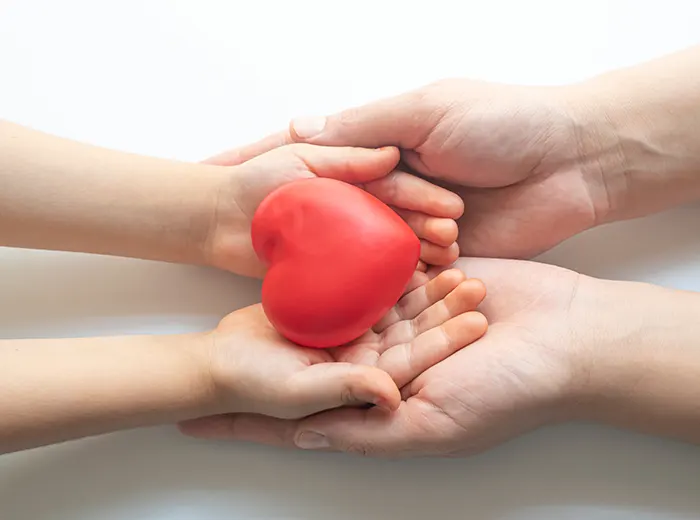 Hände halten Kinderhände mit einem roten Herz, symbolisierend Lebensmut