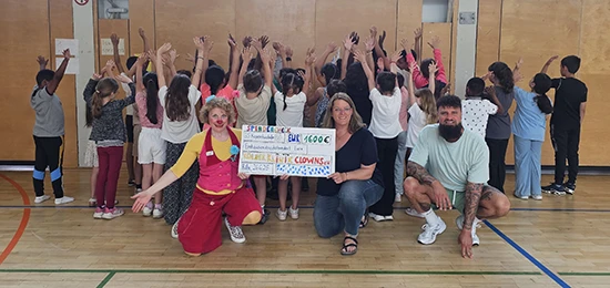 Gruppenfoto von Grundschülern und Klinik-Clown in Tunrhalle mit Check vom Spendenlauf